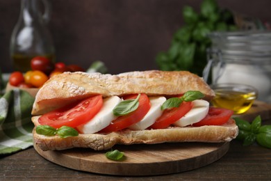 Photo of Tasty sandwich with mozzarella cheese, tomatoes and basil on wooden table against brown background, closeup