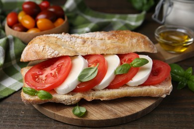Photo of Tasty sandwich with mozzarella cheese, tomatoes and basil on wooden table, closeup