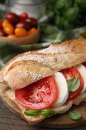 Photo of Tasty sandwich with mozzarella cheese, tomatoes and basil on wooden table, closeup