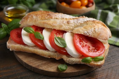 Photo of Tasty sandwich with mozzarella cheese, tomatoes and basil on wooden table, closeup
