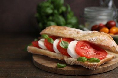 Photo of Tasty sandwich with mozzarella cheese, tomatoes and basil on wooden table against brown background, closeup