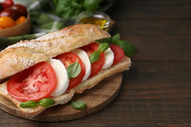 Photo of Tasty sandwich with mozzarella cheese, tomatoes and basil on wooden table, closeup. Space for text