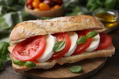 Photo of Tasty sandwich with mozzarella cheese, tomatoes and basil on wooden table, closeup