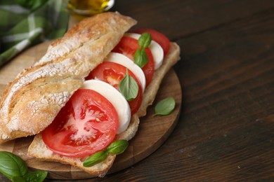 Photo of Tasty sandwich with mozzarella cheese, tomatoes and basil on wooden table, closeup. Space for text
