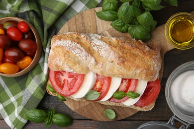 Photo of Tasty sandwich with mozzarella cheese, tomatoes and basil on wooden table, flat lay