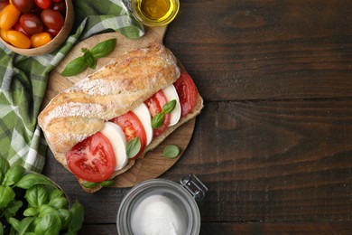 Photo of Tasty sandwich with mozzarella cheese, tomatoes and basil on wooden table, flat lay. Space for text