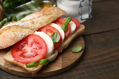 Photo of Tasty sandwich with mozzarella cheese, tomatoes and basil on wooden table, closeup
