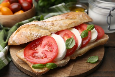 Photo of Tasty sandwich with mozzarella cheese, tomatoes and basil on wooden table, closeup