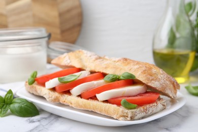 Photo of Tasty sandwich with mozzarella cheese, tomatoes and basil on white marble table, closeup