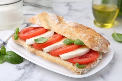 Photo of Tasty sandwich with mozzarella cheese, tomatoes and basil on white marble table, closeup