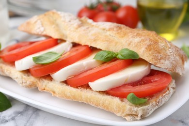 Photo of Tasty sandwich with mozzarella cheese, tomatoes and basil on white marble table, closeup