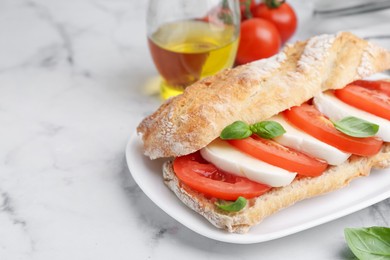 Photo of Tasty sandwich with mozzarella cheese, tomatoes and basil on white marble table, closeup. Space for text