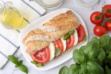Photo of Tasty sandwich with mozzarella cheese, tomatoes and basil on white marble table, flat lay