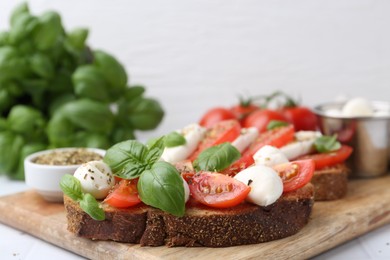 Photo of Tasty sandwiches with mozzarella cheese, tomatoes, basil and spices on light table, closeup