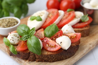 Photo of Tasty sandwiches with mozzarella cheese, tomatoes, basil and spices on light table, closeup