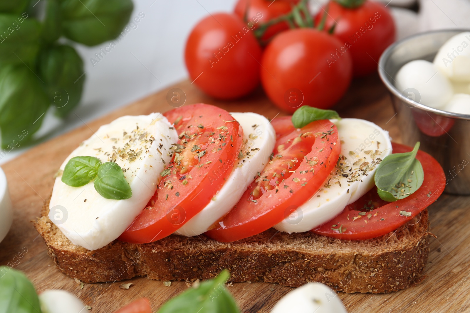 Tasty sandwich with mozzarella cheese, tomatoes, basil and spices on light table, closeup Photo of Tasty sandwich with mozzarella cheese, tomatoes, basil and spices on light table, closeup