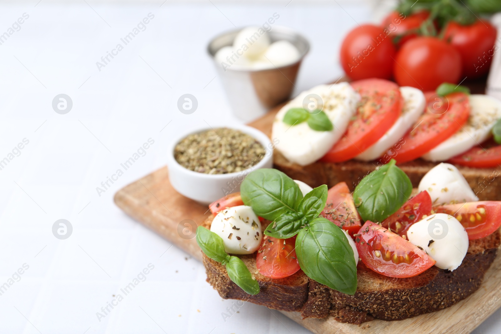 Tasty sandwiches with mozzarella cheese, tomatoes, basil and spices on light tiled table, closeup. Space for text Photo of Tasty sandwiches with mozzarella cheese, tomatoes, basil and spices on light tiled table, closeup. Space for text