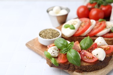 Photo of Tasty sandwiches with mozzarella cheese, tomatoes, basil and spices on light tiled table, closeup. Space for text