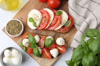 Photo of Tasty sandwiches with mozzarella cheese, tomatoes, basil and spices on light tiled table, flat lay