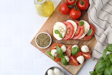 Photo of Tasty sandwiches with mozzarella cheese, tomatoes, basil and spices on light tiled table, flat lay. Space for text