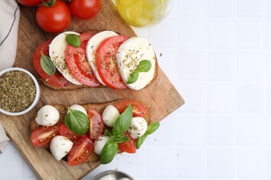 Photo of Tasty sandwiches with mozzarella cheese, tomatoes, basil and spices on light tiled table, flat lay. Space for text