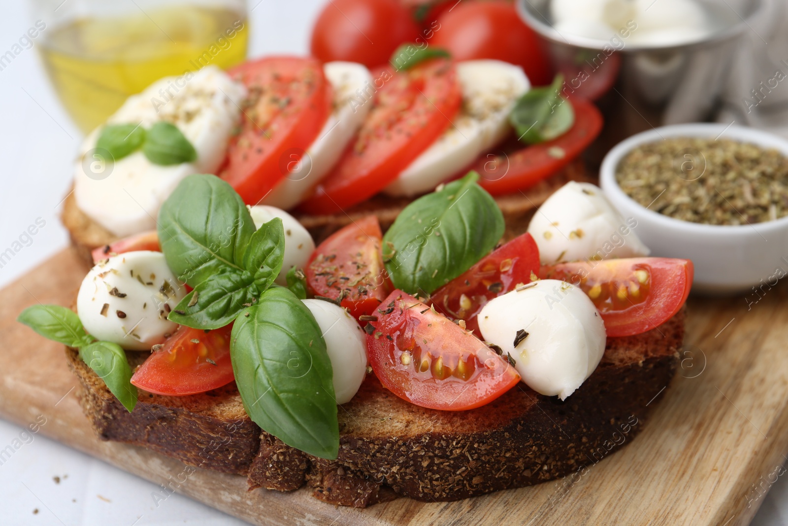 Tasty sandwiches with mozzarella cheese, tomatoes, basil and spices on light table, closeup Photo of Tasty sandwiches with mozzarella cheese, tomatoes, basil and spices on light table, closeup