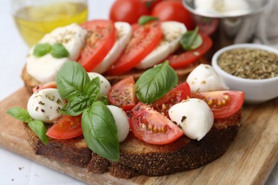 Photo of Tasty sandwiches with mozzarella cheese, tomatoes, basil and spices on light table, closeup