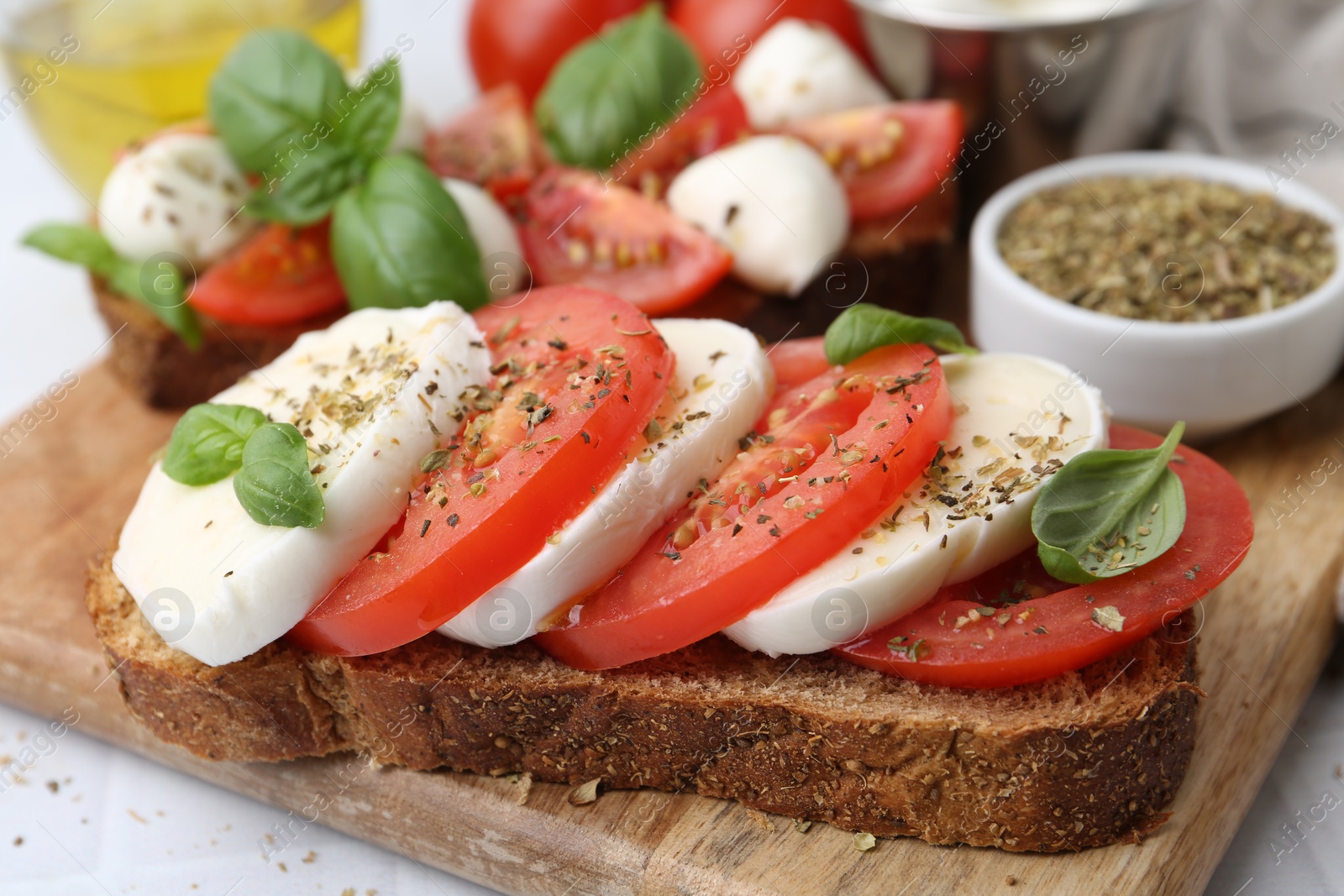 Tasty sandwiches with mozzarella cheese, tomatoes, basil and spices on light table, closeup Photo of Tasty sandwiches with mozzarella cheese, tomatoes, basil and spices on light table, closeup