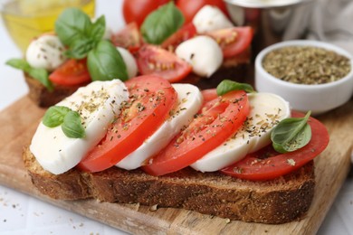 Photo of Tasty sandwiches with mozzarella cheese, tomatoes, basil and spices on light table, closeup