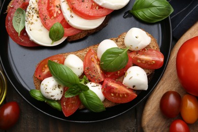 Photo of Tasty sandwiches with mozzarella cheese, tomatoes, basil and spices on wooden table, flat lay
