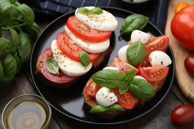 Photo of Tasty sandwiches with mozzarella cheese, tomatoes, basil and spices on wooden table, closeup