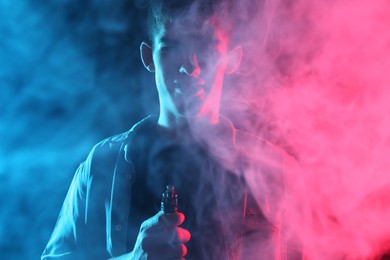 Photo of Man using electronic smoking device in neon lights on dark background