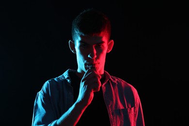 Photo of Man using electronic smoking device in neon lights on black background