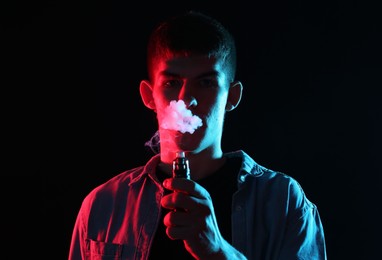 Photo of Man using electronic smoking device in neon lights on black background