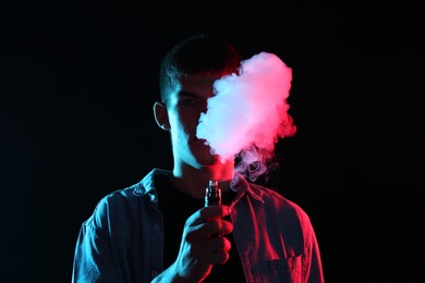 Photo of Man using electronic smoking device in neon lights on black background