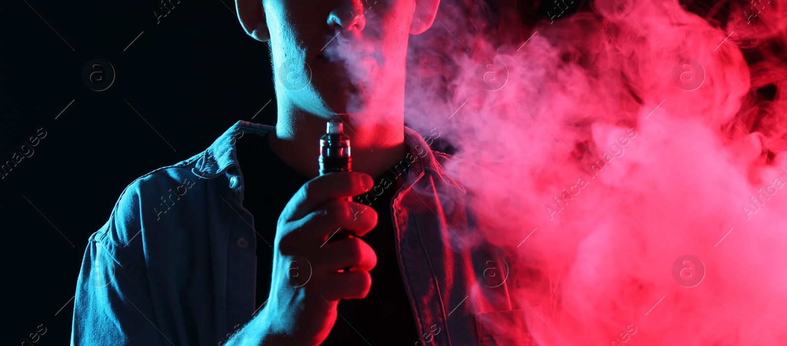 Man using electronic smoking device in neon lights on black background, closeup Photo of Man using electronic smoking device in neon lights on black background, closeup