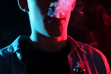 Photo of Man using electronic smoking device in neon lights on black background, closeup