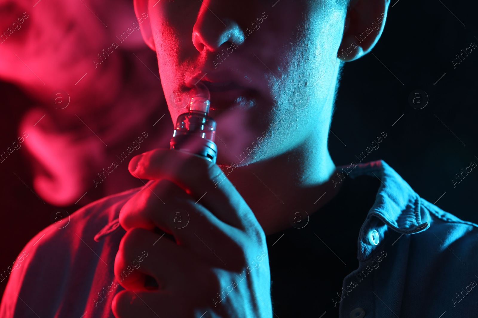 Man using electronic smoking device in neon lights on black background, closeup Photo of Man using electronic smoking device in neon lights on black background, closeup