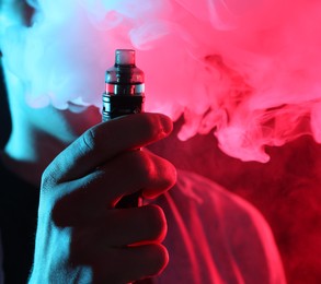 Photo of Man using electronic smoking device in neon lights on dark background, closeup