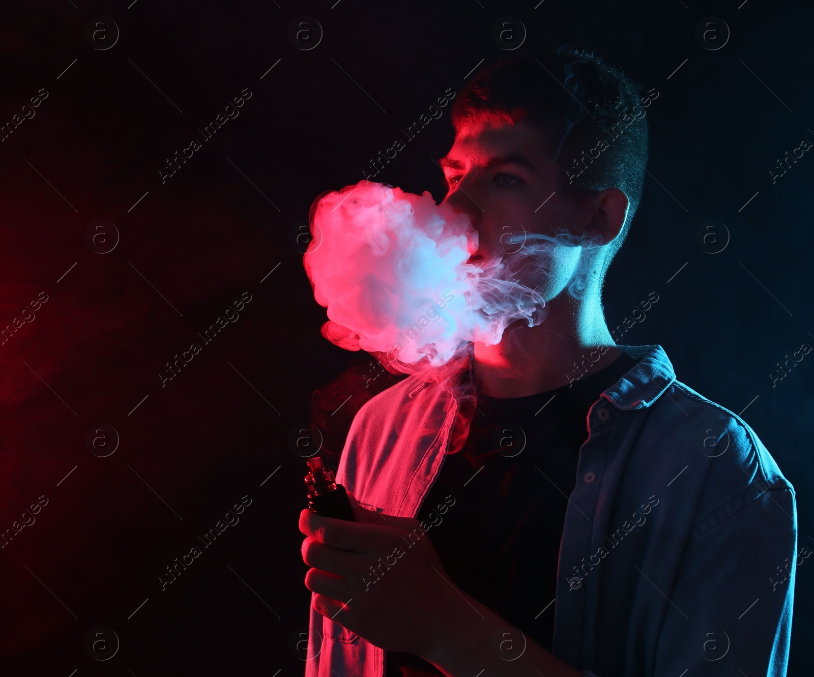 Man using electronic smoking device in neon lights on dark background, space for text Photo of Man using electronic smoking device in neon lights on dark background, space for text
