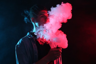 Photo of Man using electronic smoking device in neon lights on dark background