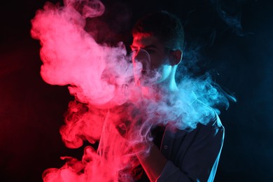 Photo of Man using electronic smoking device in neon lights on dark background