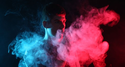 Photo of Man using electronic smoking device in neon lights on dark background