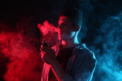 Photo of Man using electronic smoking device in neon lights on dark background