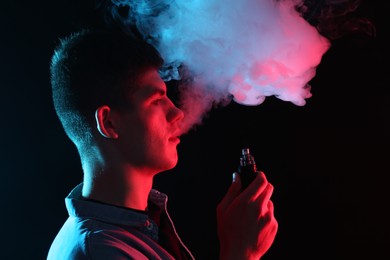 Photo of Man using electronic smoking device in neon lights on black background