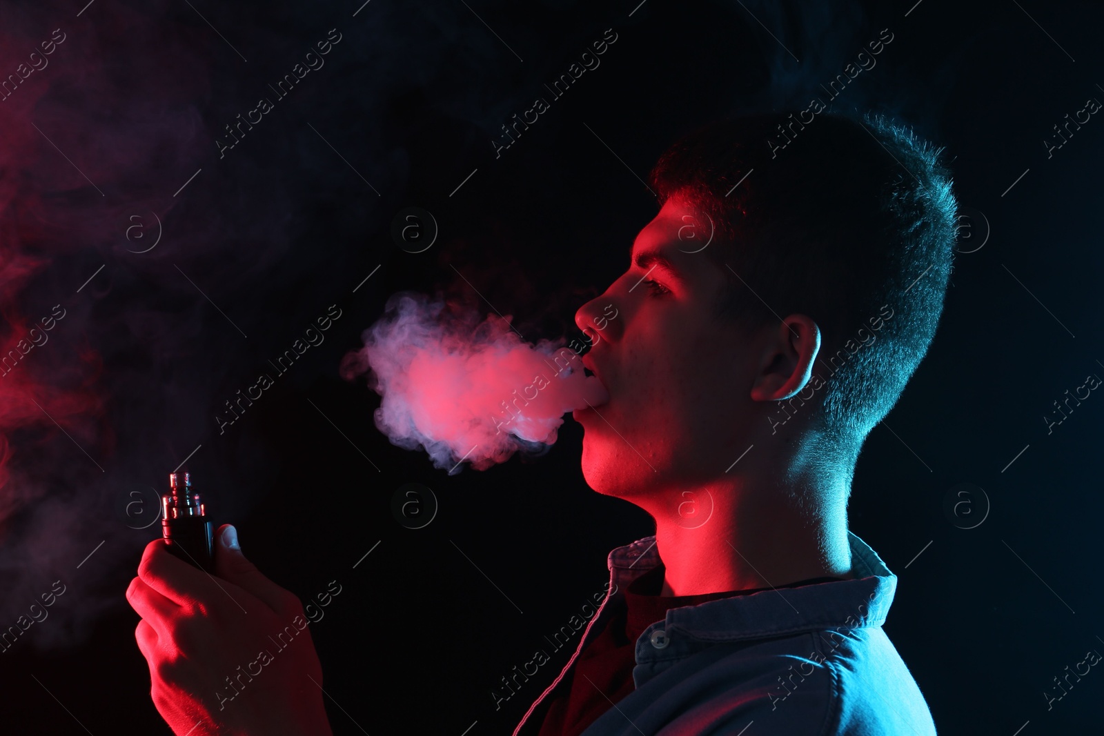 Man using electronic smoking device in neon lights on black background Photo of Man using electronic smoking device in neon lights on black background