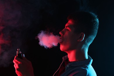 Photo of Man using electronic smoking device in neon lights on black background