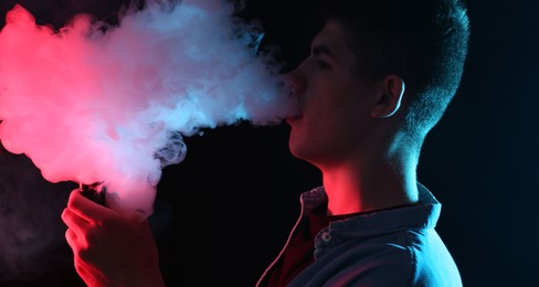 Photo of Man using electronic smoking device in neon lights on black background