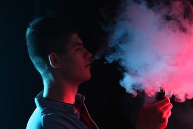 Photo of Man using electronic smoking device in neon lights on black background