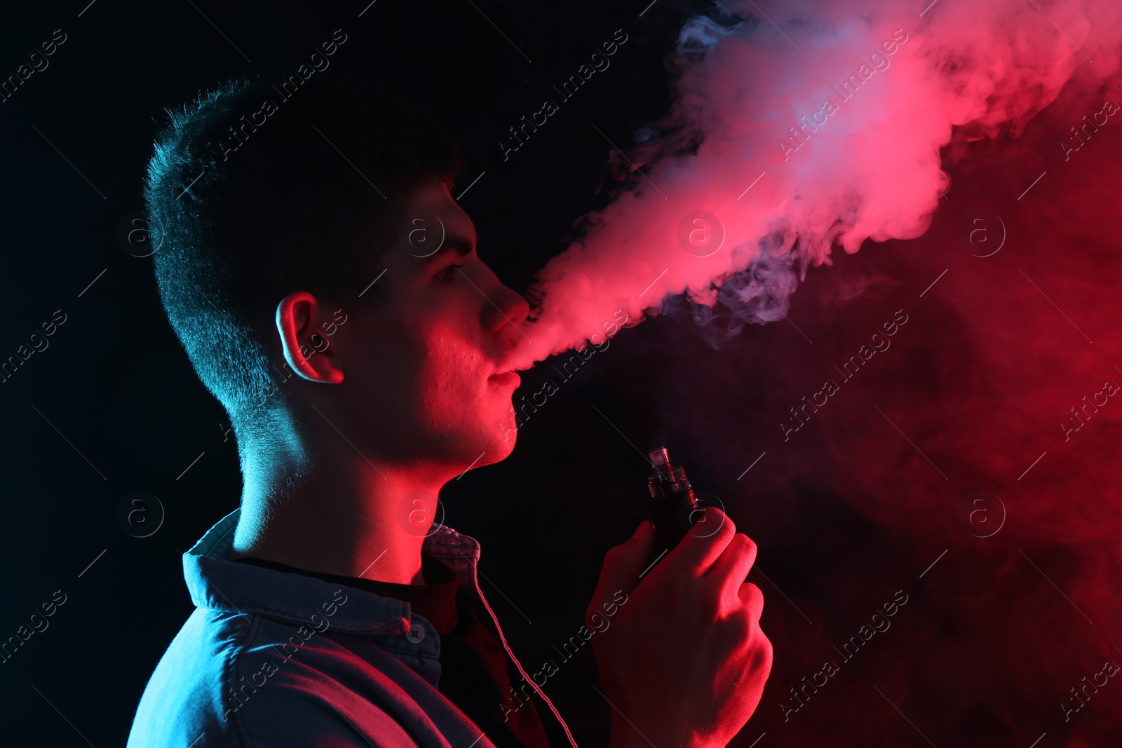 Man using electronic smoking device in neon lights on black background Photo of Man using electronic smoking device in neon lights on black background